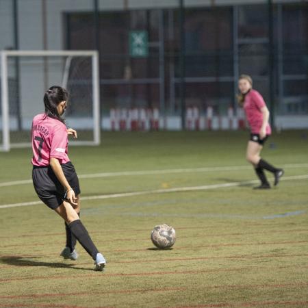 Een meisje schopt een voetbal op voetbalveld naar een andere speler